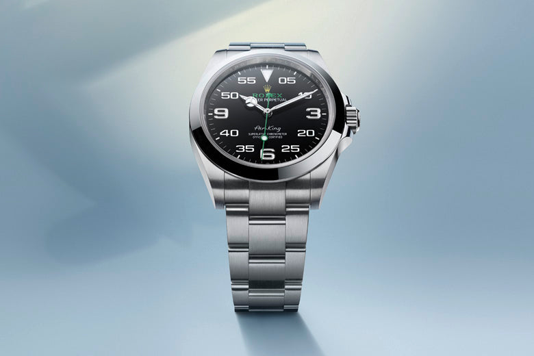 A sleek, silver wristwatch with a metallic band on a gradient blue background. The watch face is black with white numerals indicating hours and minutes in a modern font, and the hands are also silver. A soft light shines from the top left corner.