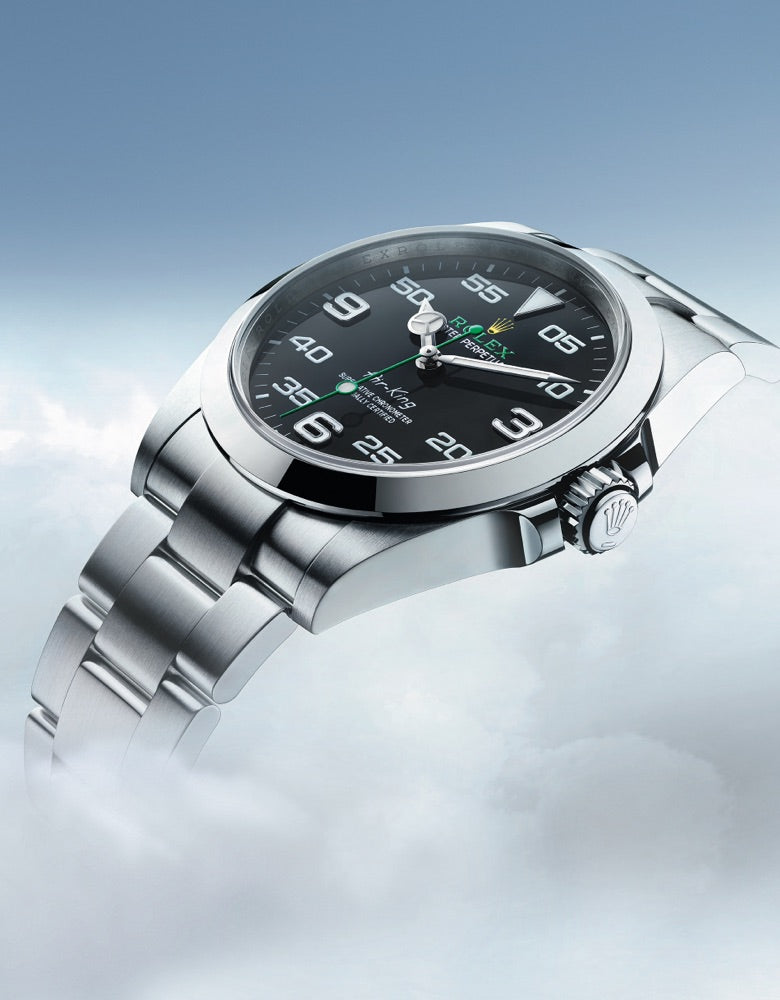 A sleek silver wristwatch with a dark face displaying white Arabic numerals and green accents floats above a cloud-filled sky, highlighting its polished metallic band and modern design against the serene, airy background.