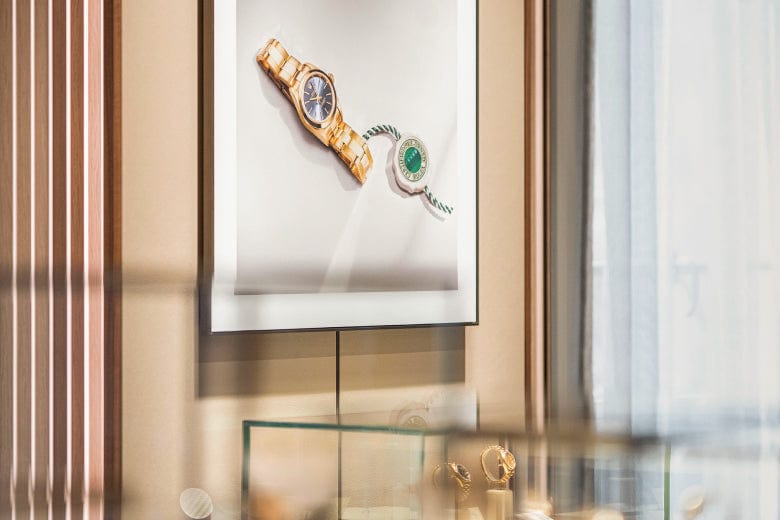 Framed image of two watches on a wall, with glass display cases containing jewelry below.