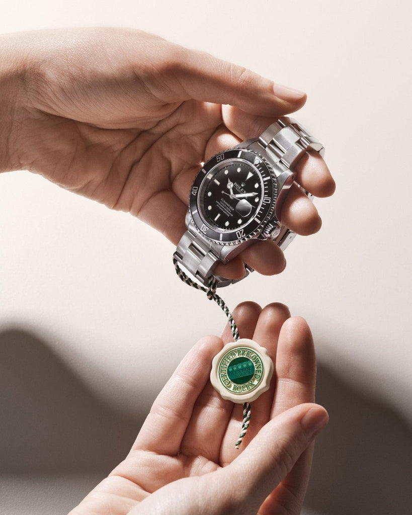 Hands holding a silver wristwatch with a black dial and a green tag.