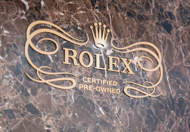 Rolex Certified Pre-Owned sign with gold lettering and logo on a marble background.