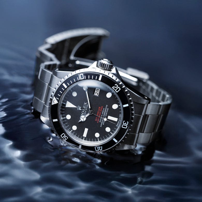 A stainless steel dive watch with a black dial and white hour markers is partially submerged in rippling water.