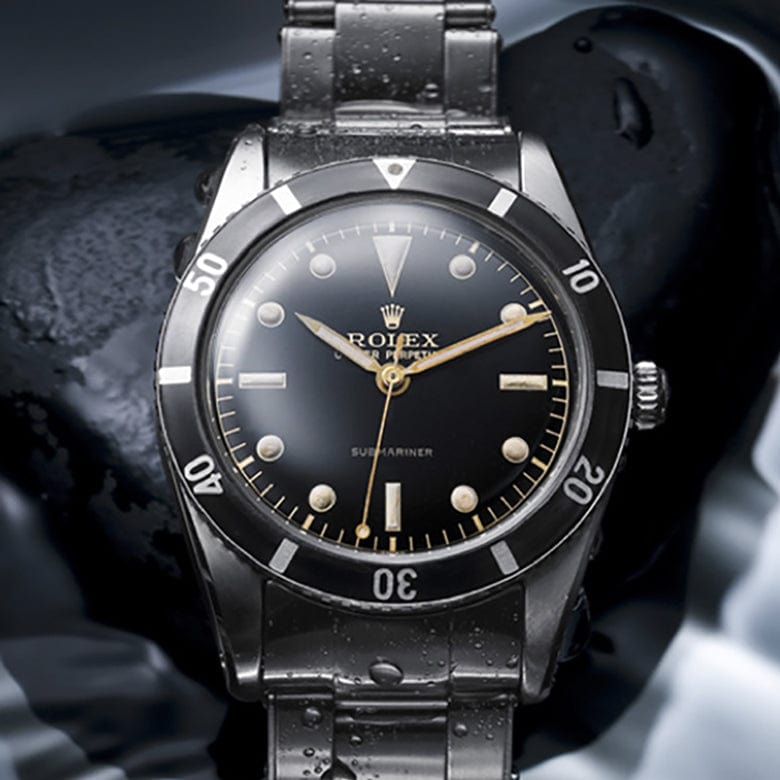 Black and silver luxury diving watch with luminescent markers and rotating bezel, displayed on a wet, textured surface.