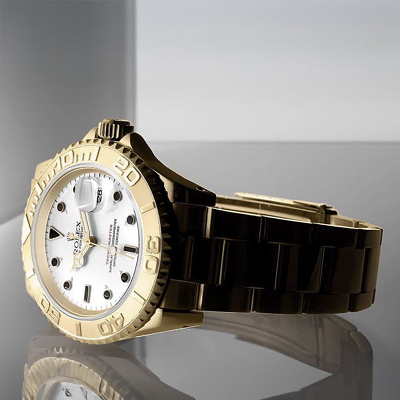 Gold wristwatch with a white face, black accents, and a metallic band, displayed on a reflective gray surface.