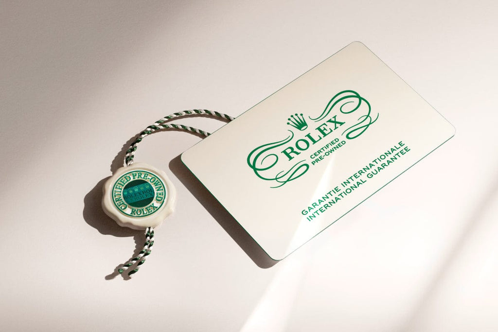 A Rolex certification card and a green and white tag are shown on a light surface.