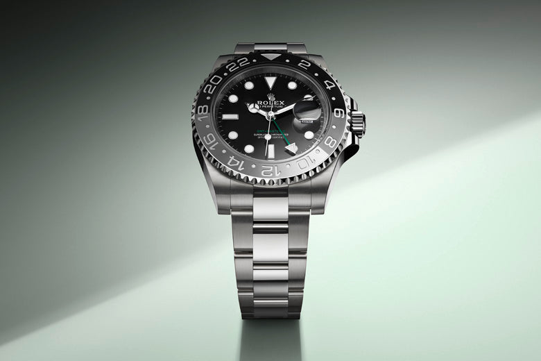 A luxury wristwatch with a silver metal band and a black dial is centered on the display. The watch has a luminous face and hands with a date feature. The background fades from dark to light green with a spotlight effect highlighting the timepiece.