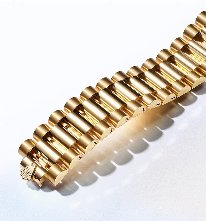 A close-up view of a luxurious gold bracelet with cylindrical links on a light background. The bracelet showcases a meticulously crafted design and elegant shine, casting soft shadows that add depth and dimension to the image.