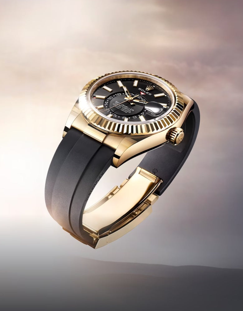 A luxurious gold and black watch with a black leather strap is poised against a soft, cloudy background. The watch face features gold hour markers and hands, and notable detailing on the bezel. Light reflects off the polished metal, highlighting its elegance.